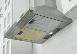 Metal range hood over cooktop with white cupboards
