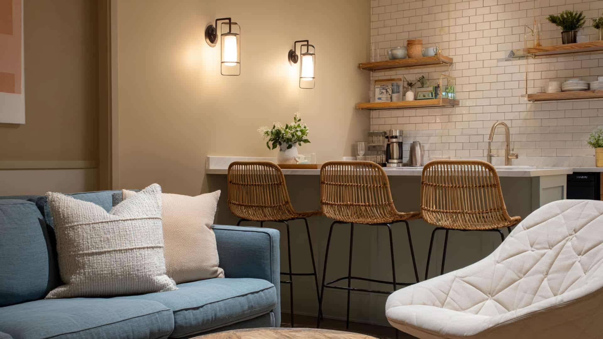 Minimal open-plan kitchen and living area with woven stools, soft blue sofa, and simple functional decor.