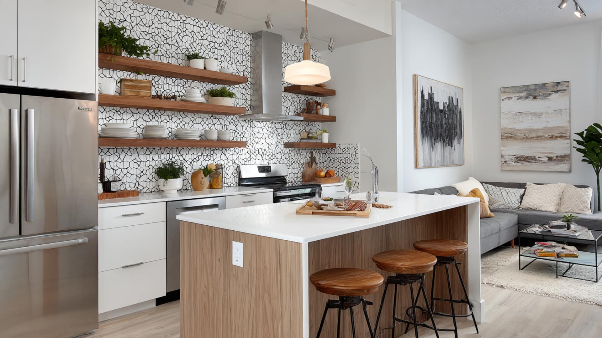 Open-plan kitchen and living room with minimalist decor, white island, floating wood shelves, and neutral sectional sofa.