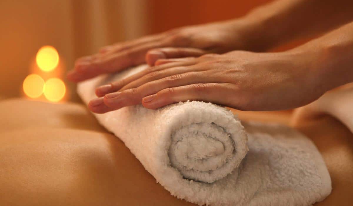 Hands placing warm white towel on back during massage