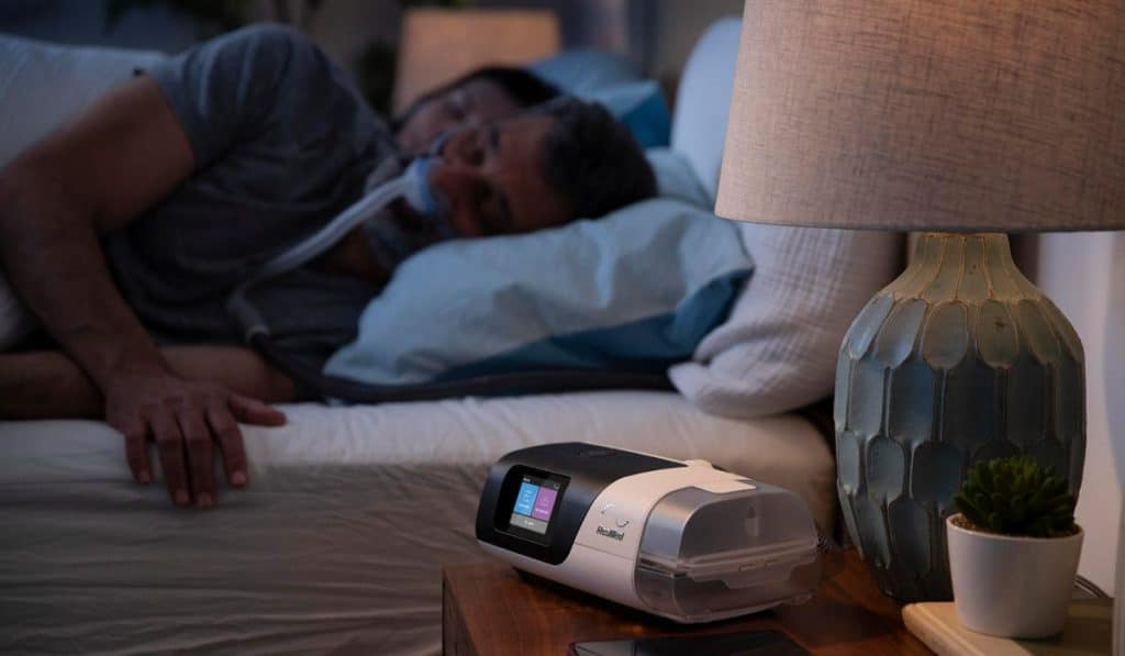 CPAP machine on nightstand with man sleeping in background