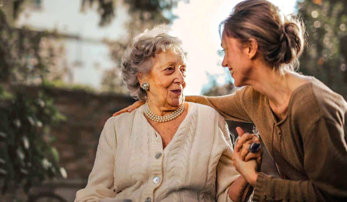 Caregiver holding hands and talking with elderly woman outdoors