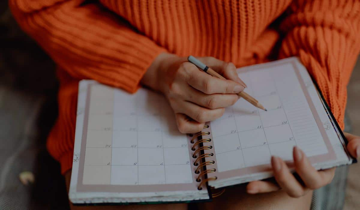 Woman in orange sweater writing in spiral calendar planner