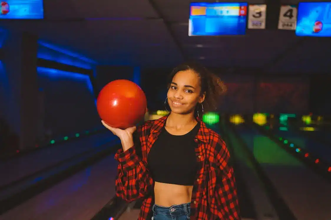 Young woman holding red bowling ball in vibrant bowling alley with neon lights