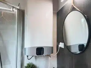 Modern electric water heater with digital controls next to round mirror in bathroom