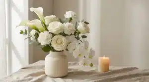 White floral arrangement in ceramic vase next to lit candle on linen-covered table
