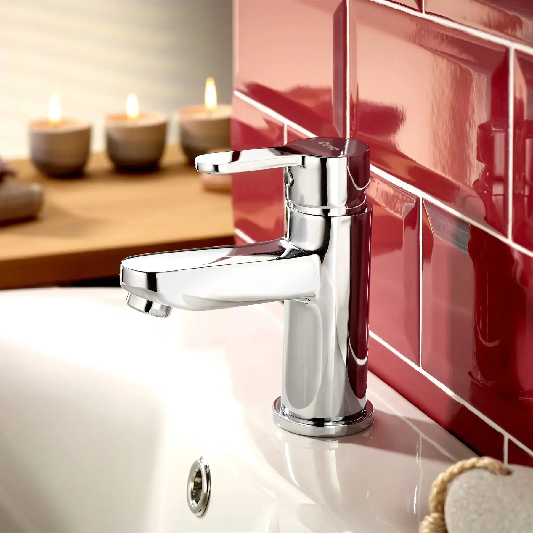 Chrome faucet on white sink against glossy red tiled wall with candles in background