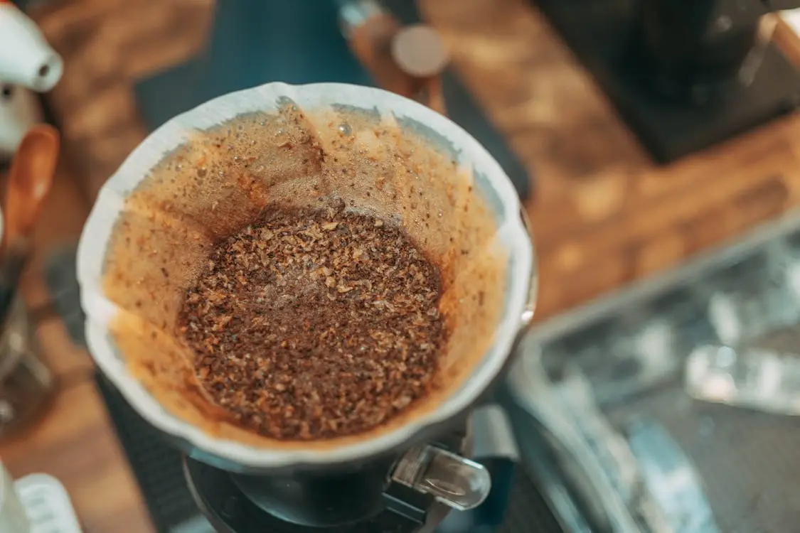 Freshly brewed coffee grounds in a filter over a drip coffee maker in a kitchen setting