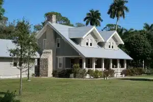 Classic gray cottage with stone chimney and wide porch in lush garden setting