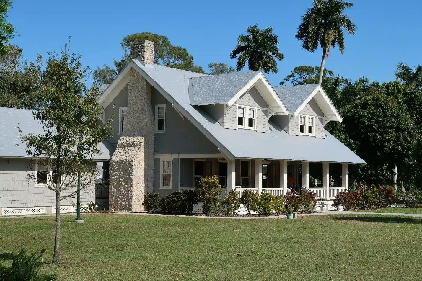 Classic gray cottage with stone chimney and wide porch in lush garden setting