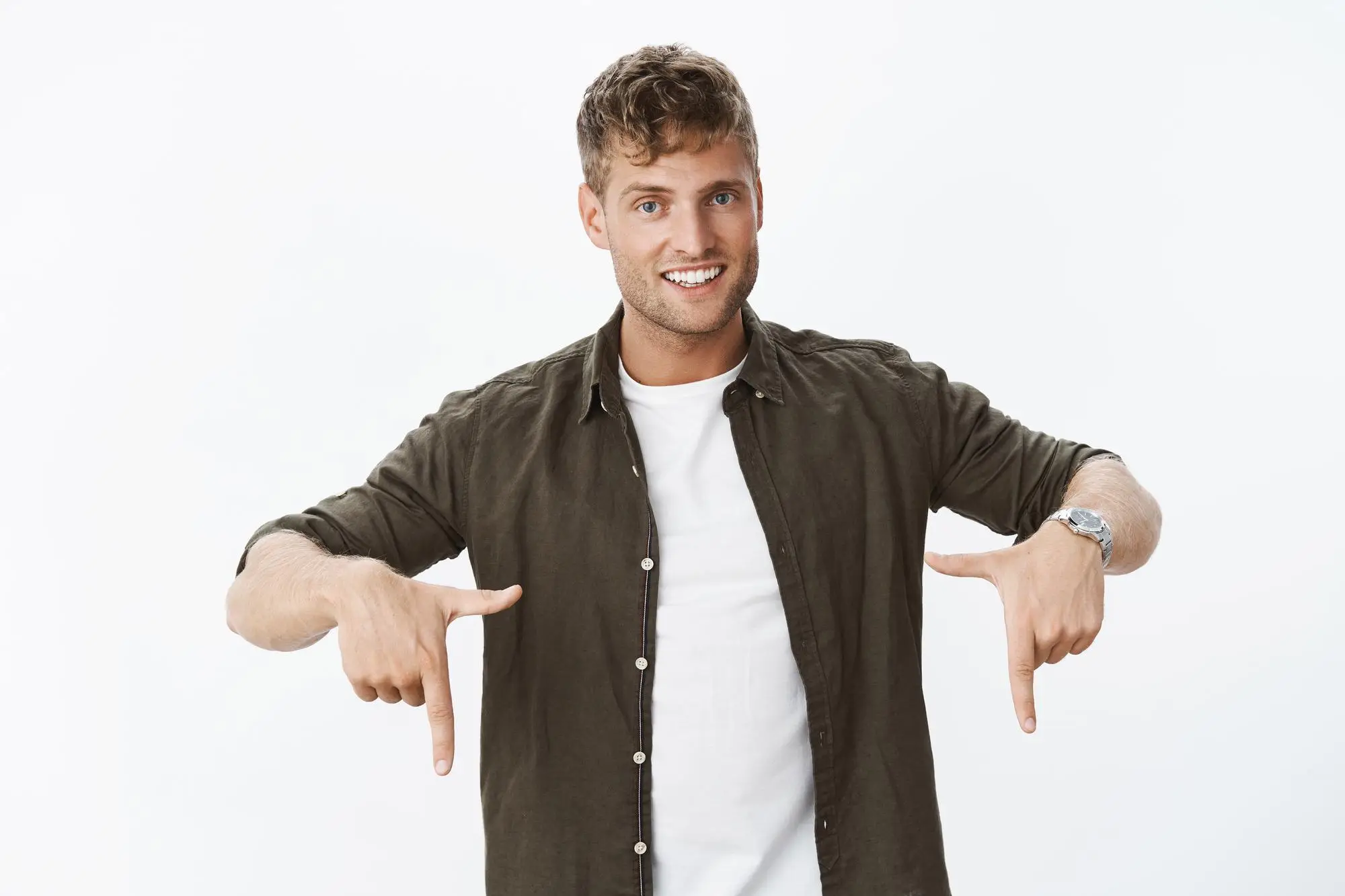 Man in green shirt and white t-shirt pointing downward on white background