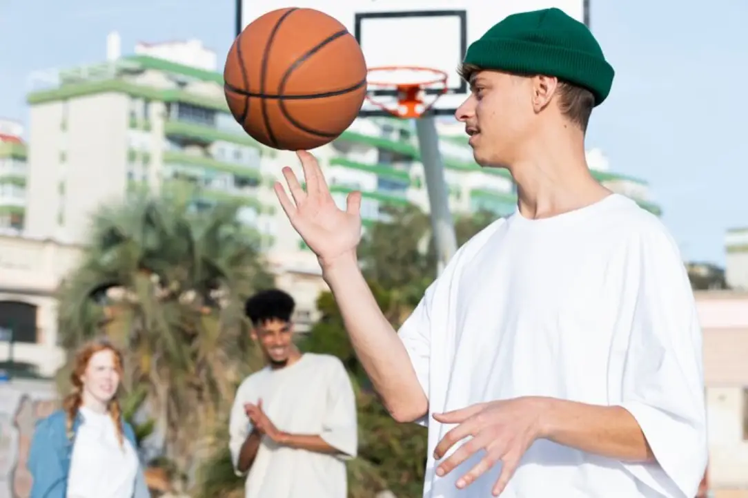 Person in white T-shirt spinning basketball on finger outdoors with friends in background