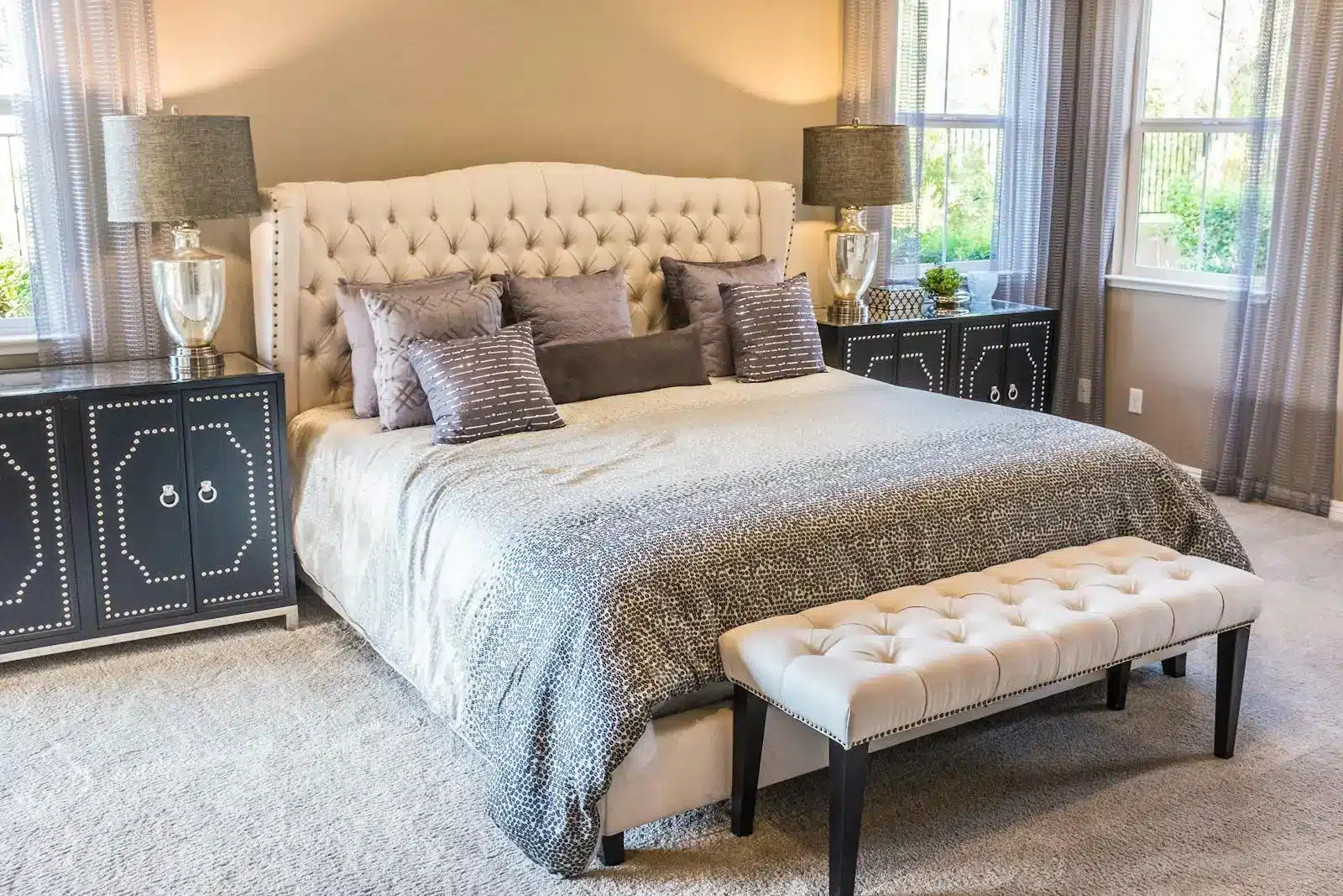 Elegant beige and gray bedroom with upholstered bed, nightstands, and tufted bench under soft lighting