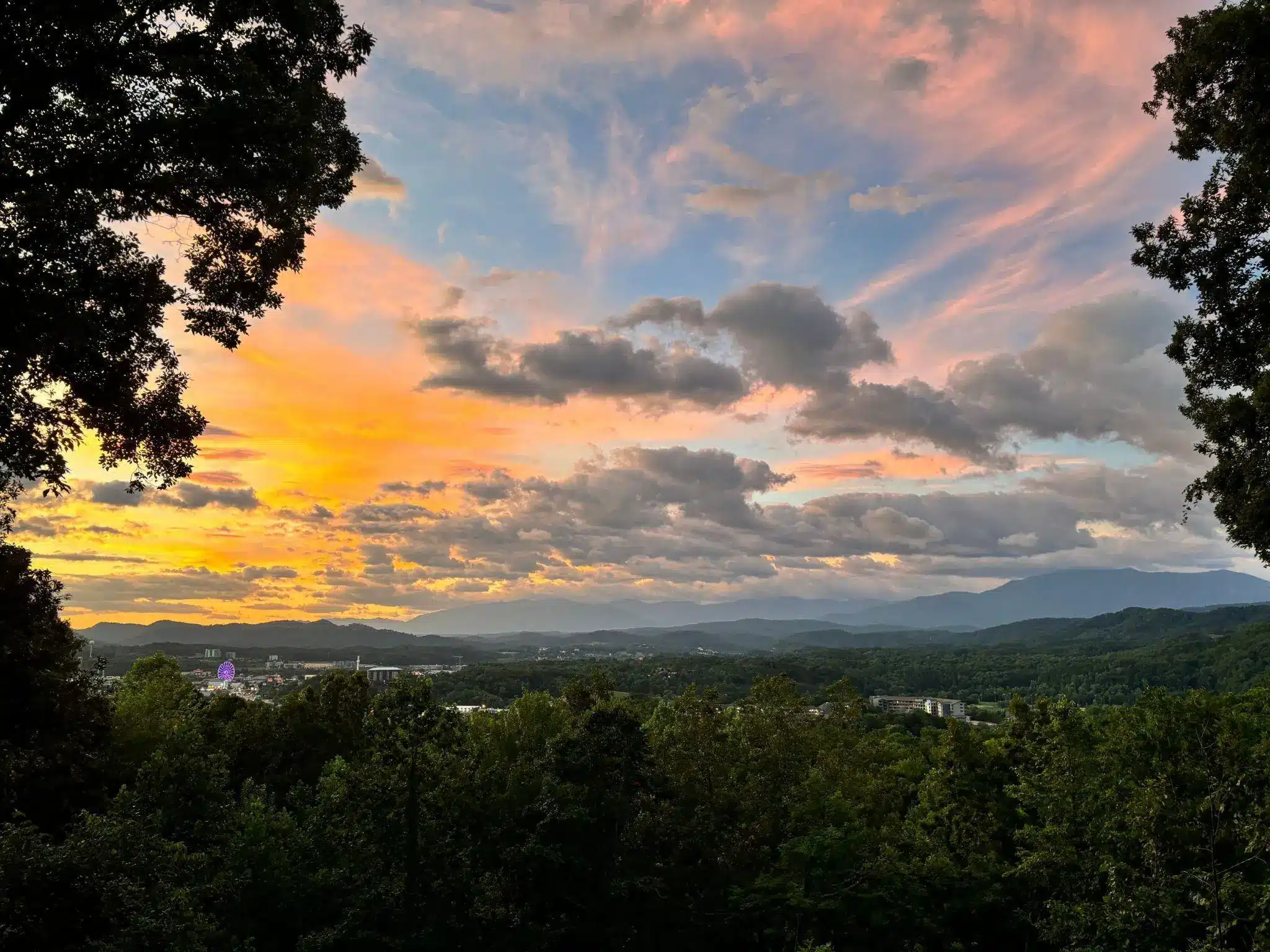 Vibrant sunset sky over forested mountains with silhouetted trees framing the view