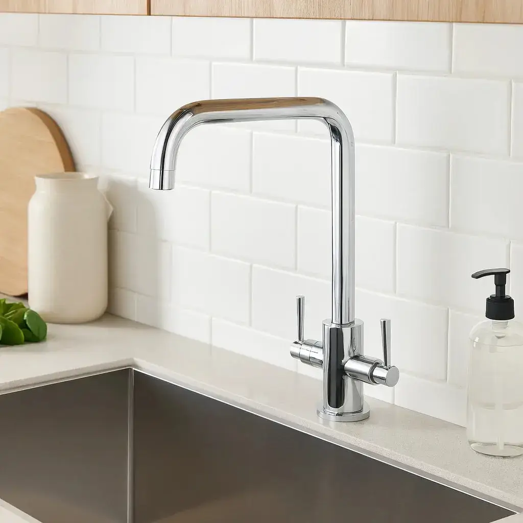 Chrome kitchen faucet over stainless steel sink next to white ceramic backsplash