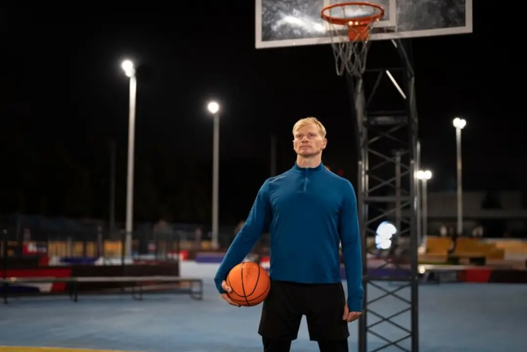 Man holding basketball under hoop on outdoor court at night