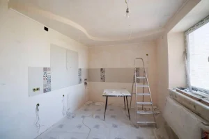 Unfinished kitchen renovation with bare walls, tile accents, and metal ladder in bright natural light