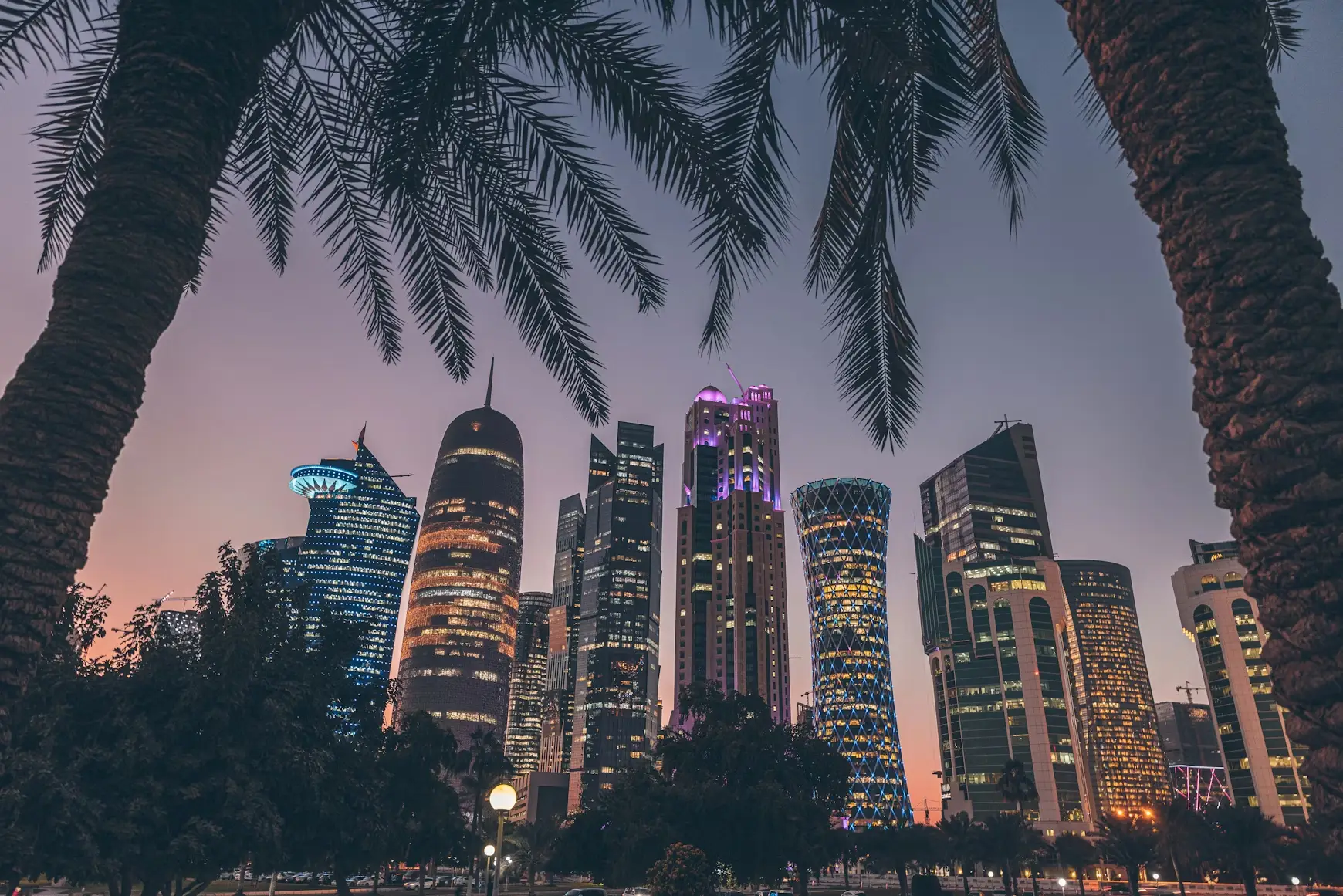 Skyscrapers with illuminated windows at dusk framed by palm trees