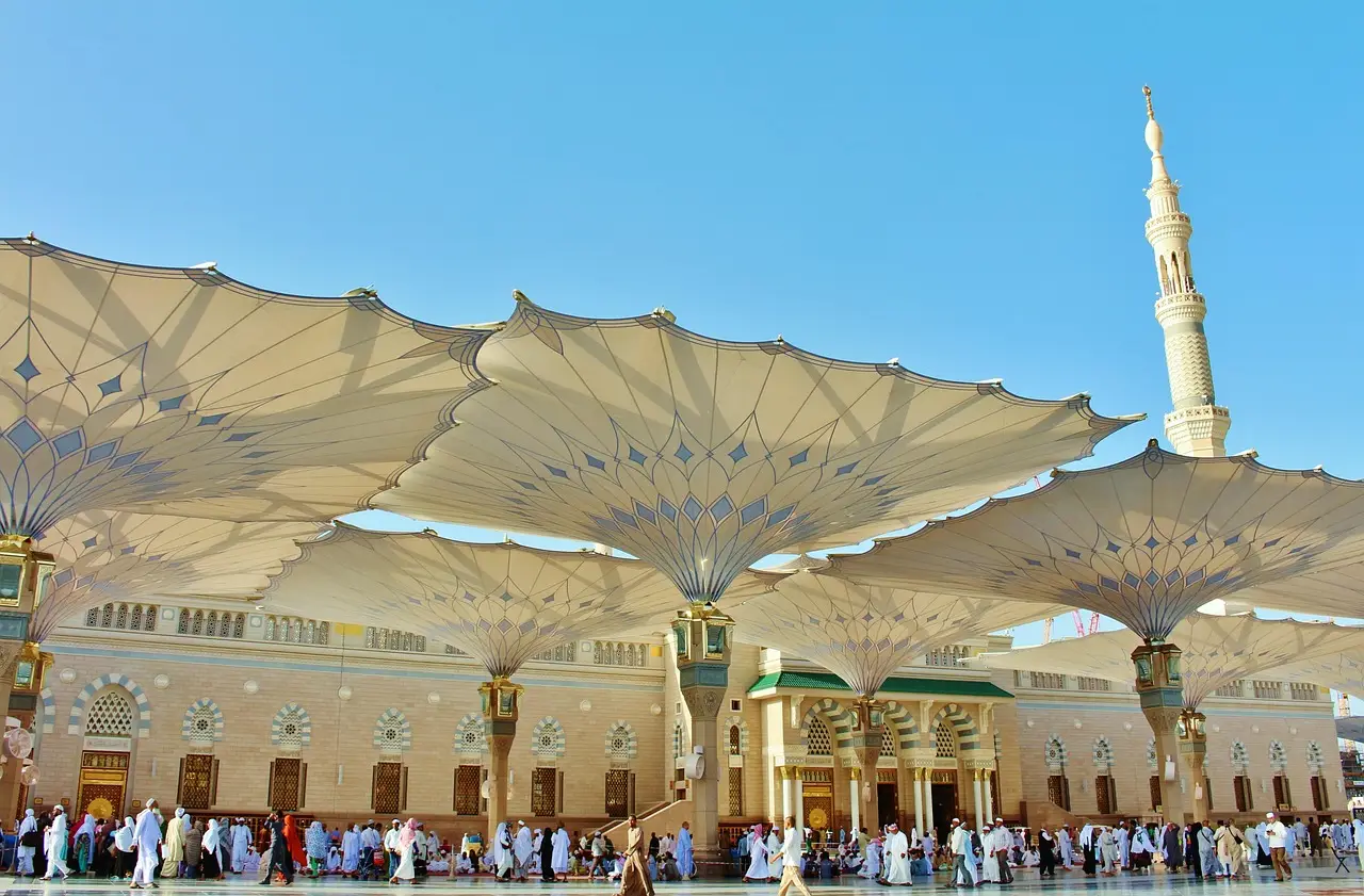 Large architectural umbrellas in courtyard with people gathering under clear blue sky