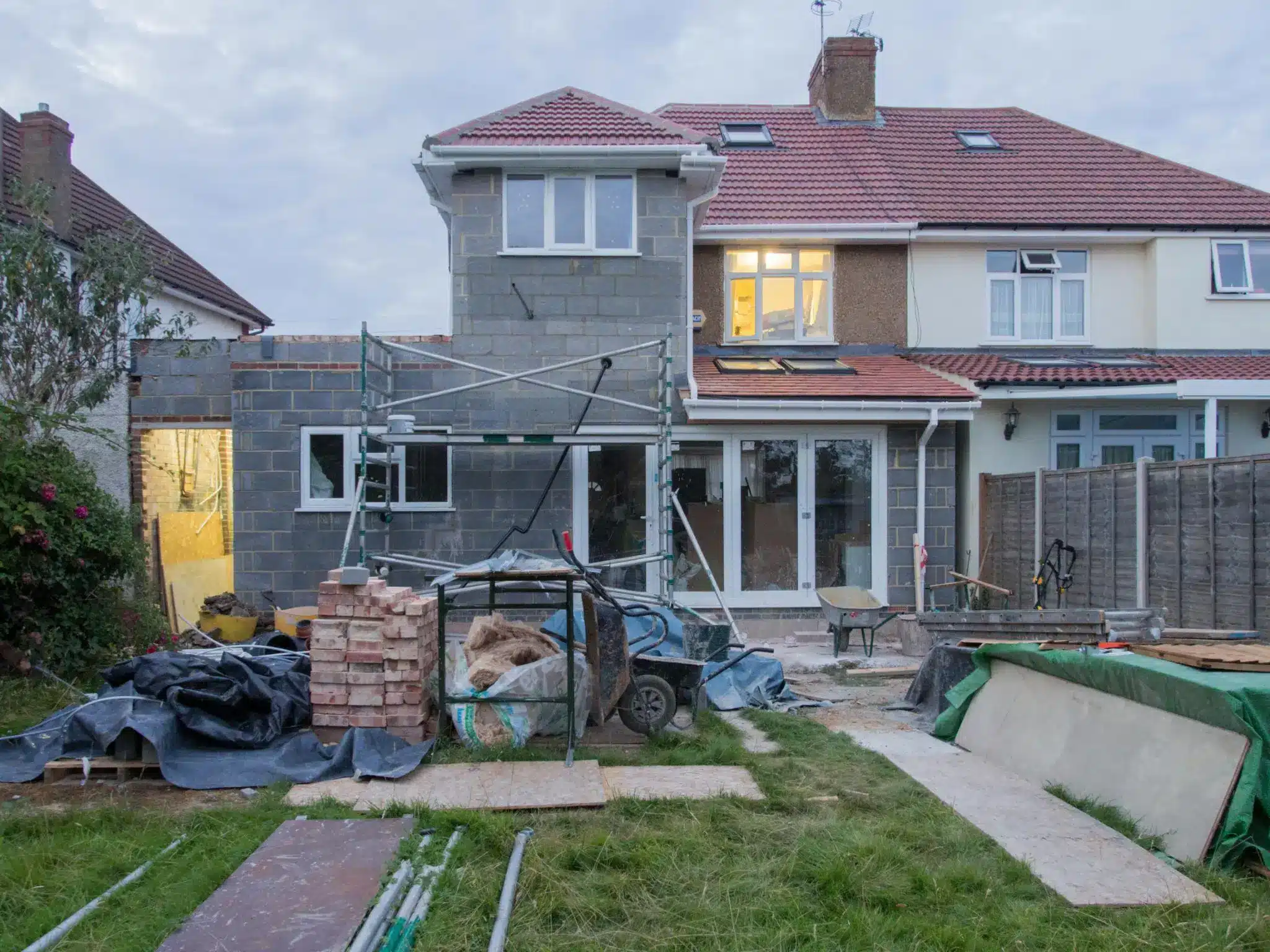 House under renovation with scaffolding, bricks, and building materials in a backyard construction site