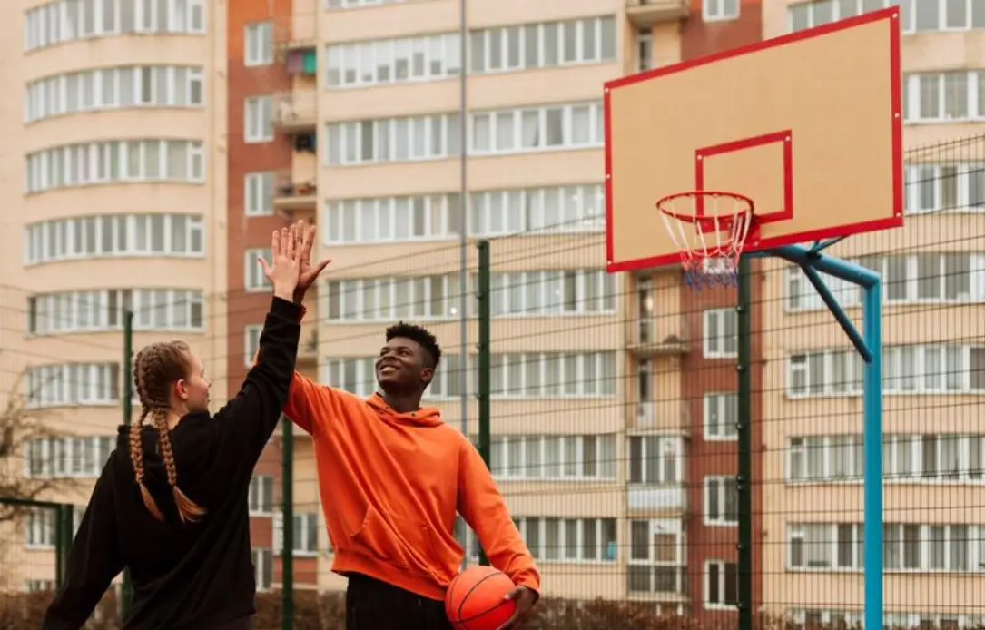 Two people high-fiving on outdoor basketball court holding basketball near urban apartment buildings