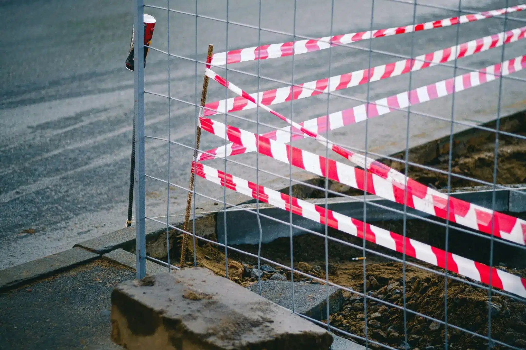 Construction site with red and white safety tape on metal fence and exposed soil