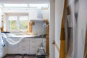 Kitchen renovation with protective plastic covers and ladders under natural light from window