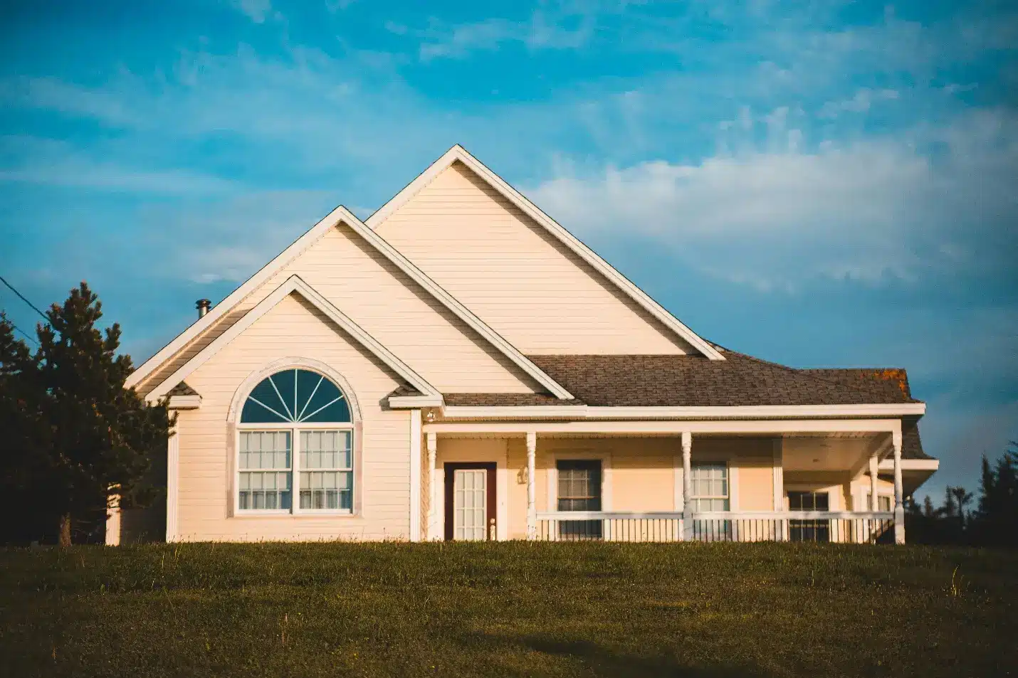Cream-colored house with large front window and porch under blue sky