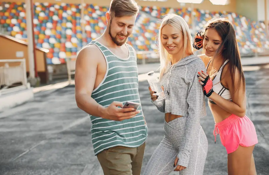 Young man and two women in athletic wear viewing smartphone at outdoor stadium track