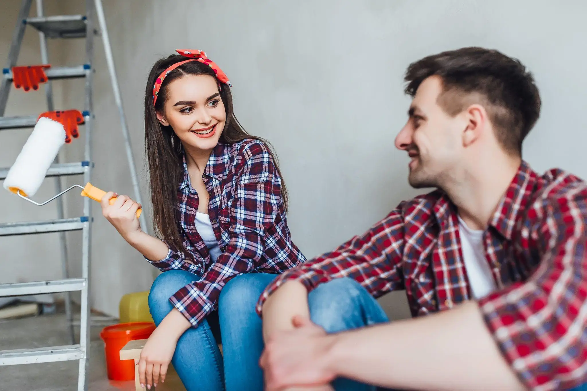 Couple in plaid shirts sitting by ladder with paint roller in hand