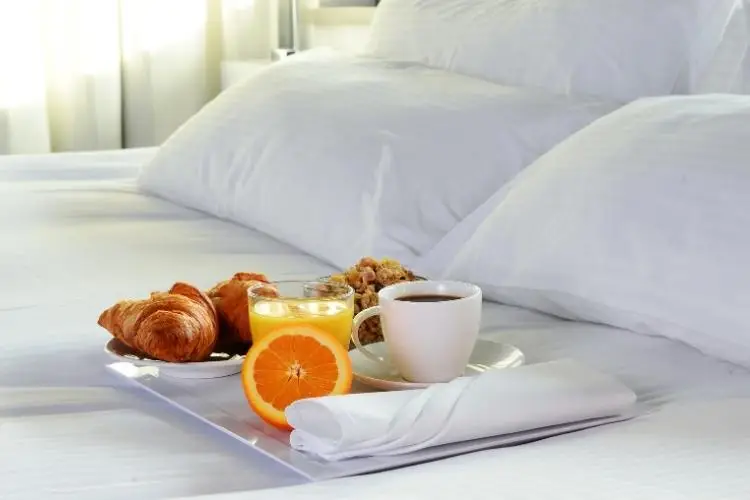 Breakfast tray with coffee, orange juice, and pastries on white bed linens