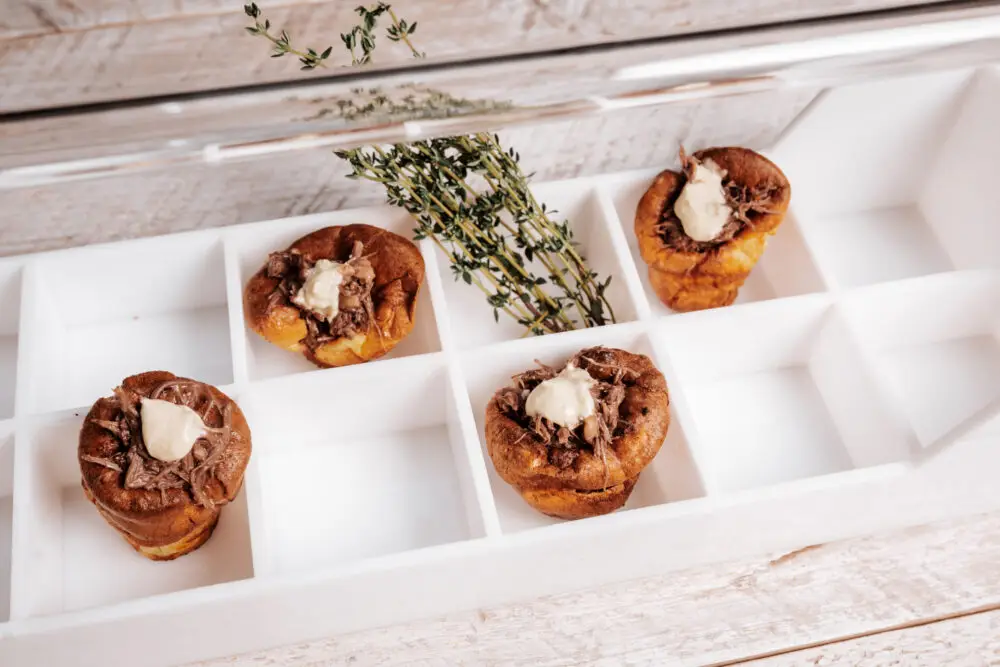 Yorkshire puddings filled with shredded beef and cream in white serving tray with fresh thyme sprigs