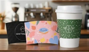 Coffee cup with green sleeve on wooden counter next to two colorful cup sleeves in a cafe