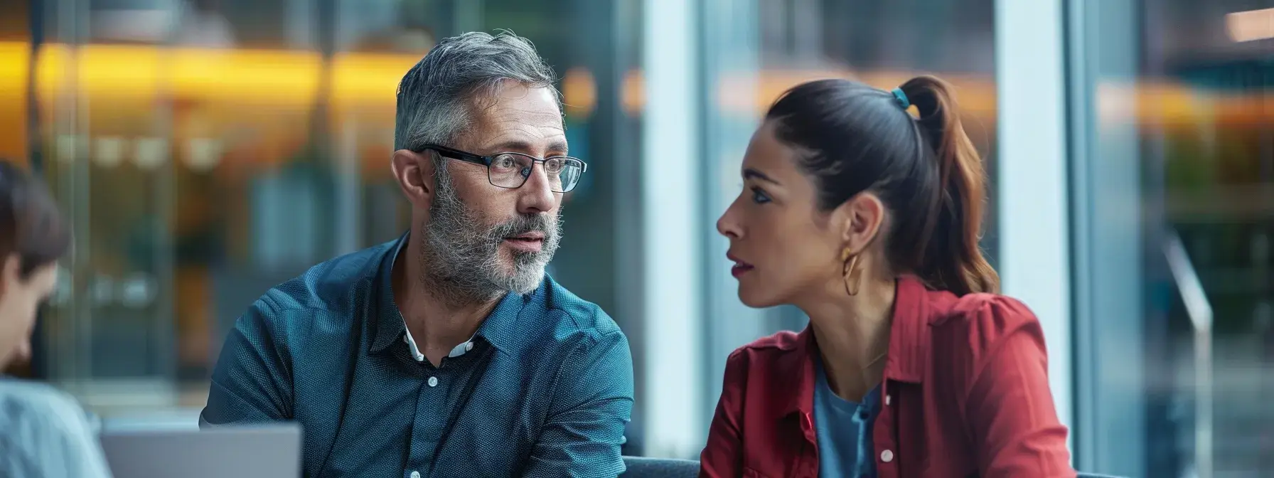 Two people engaged in conversation at an office table under soft indoor lighting
