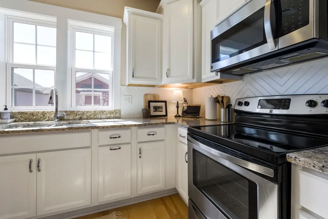 Modern kitchen with white cabinets, stainless steel appliances, and granite countertops under natural light