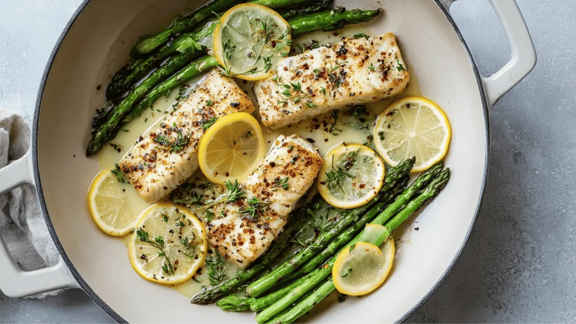 pan-seared mahi mahi fillets with asparagus and lemon slices, served in a white pan on a light gray background