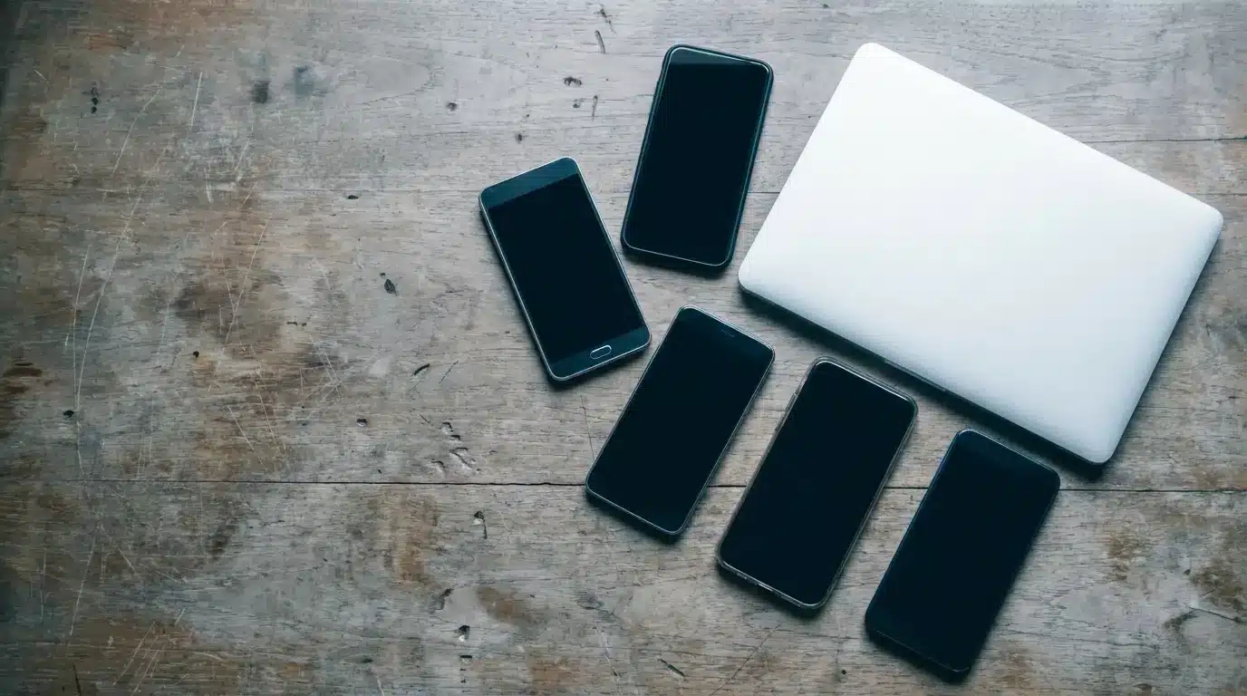 Laptop and five smartphones on scratched wooden surface in soft natural light