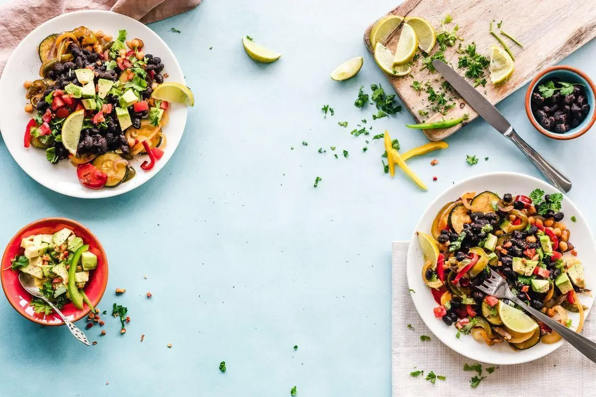 Colorful vegetable and bean salad with lime wedges on a light blue surface