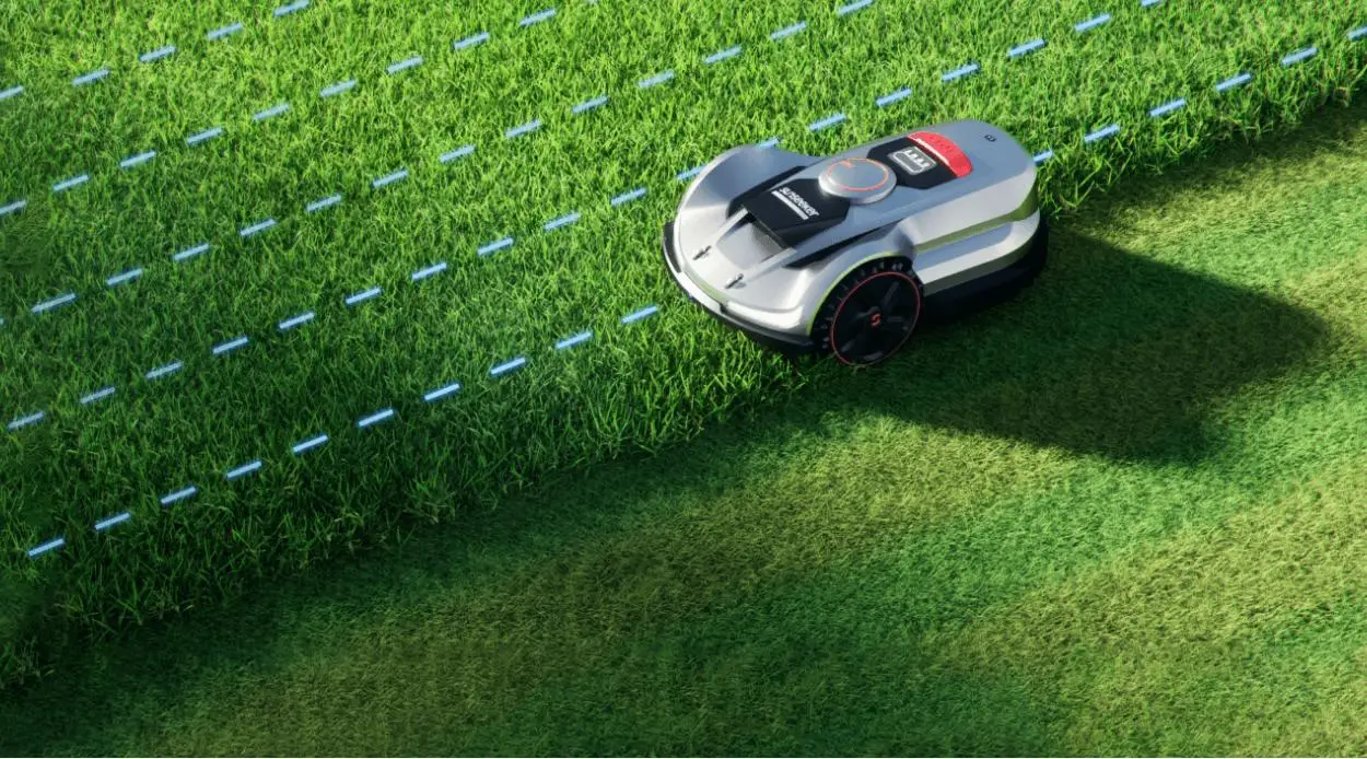 Robotic lawn mower cutting grass on a sunny day with visible tire tracks