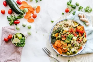 Quinoa and roasted vegetables in a bowl with fresh ingredients on a white surface