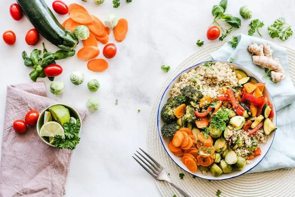 Quinoa and roasted vegetables in a bowl with fresh ingredients on a white surface