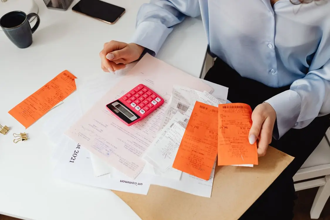 Person calculating expenses with a pink calculator and receipts on a white desk