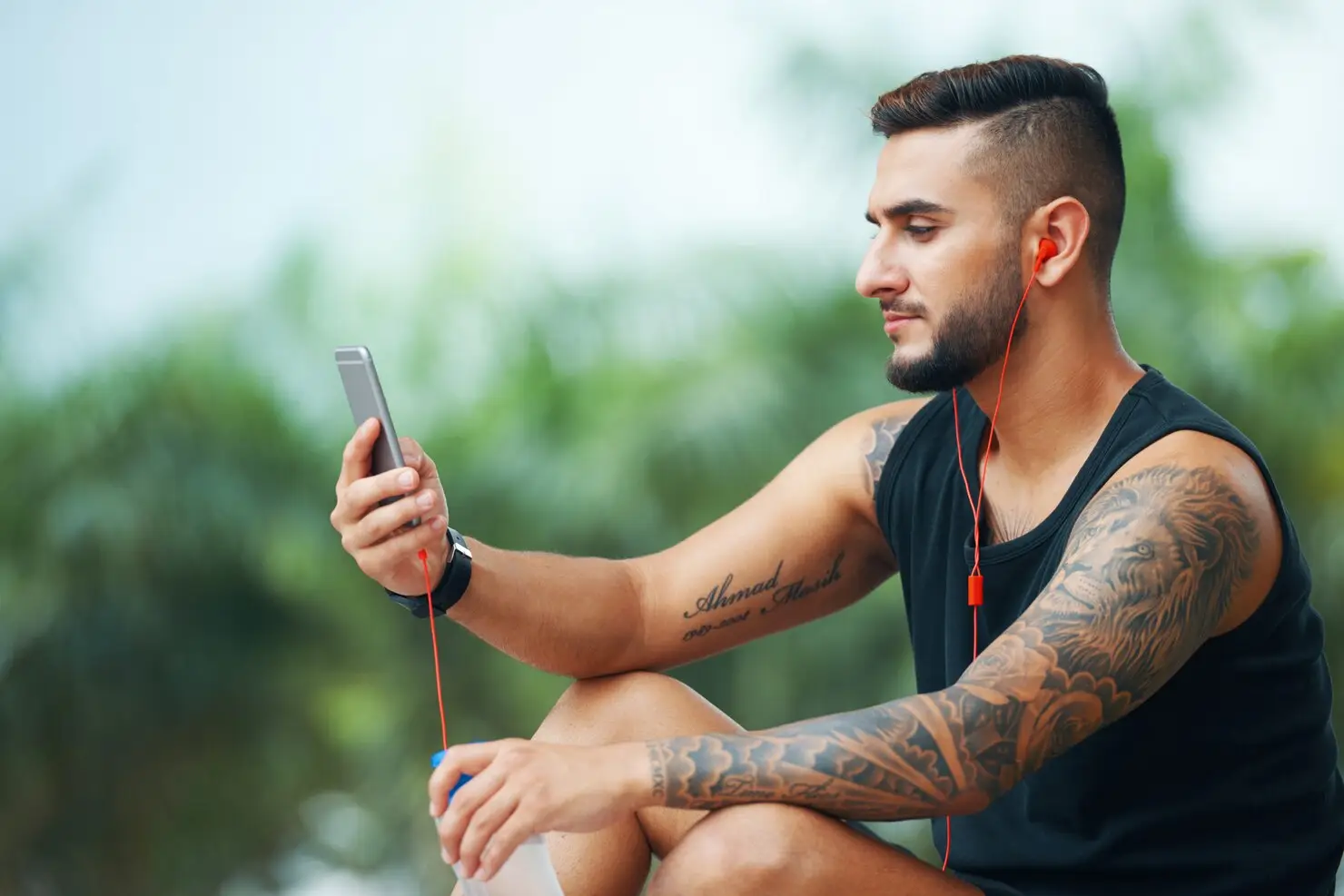 Man in black sleeveless shirt using smartphone with red earphones outdoors
