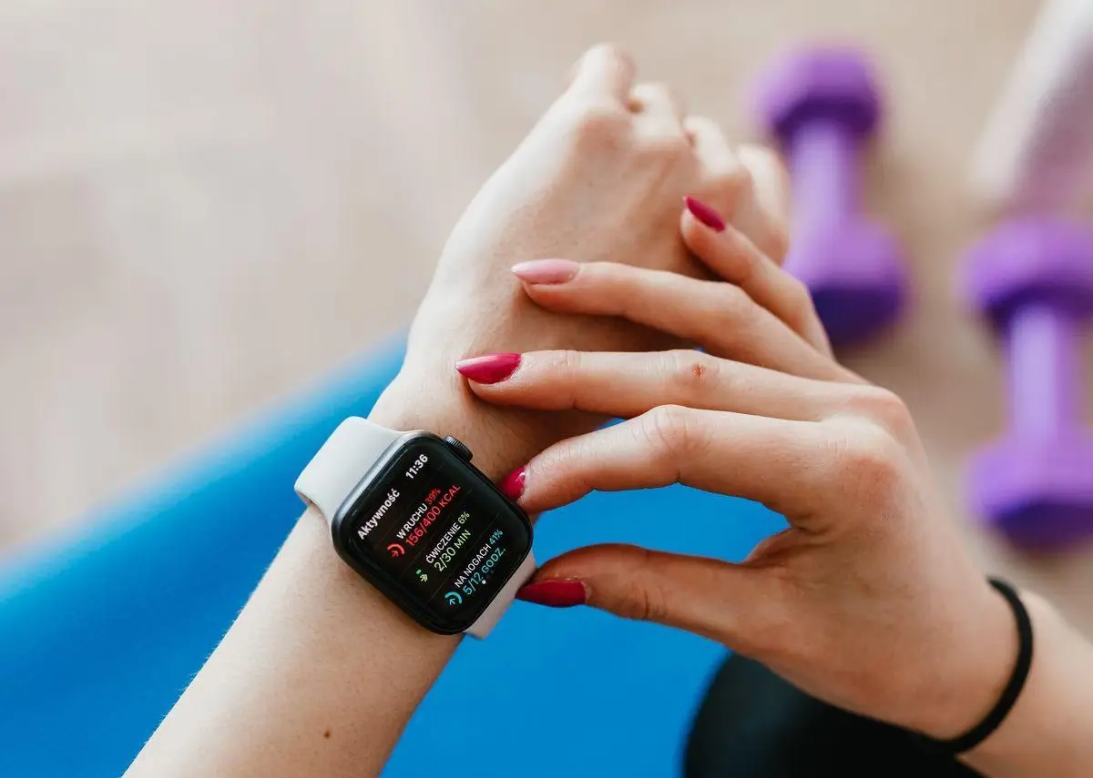 Smartwatch on wrist displaying fitness data with purple dumbbells in the background