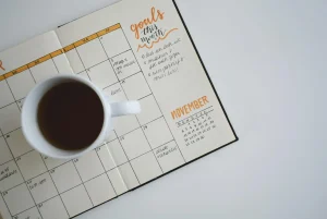 Open planner with handwritten notes and coffee cup on white table