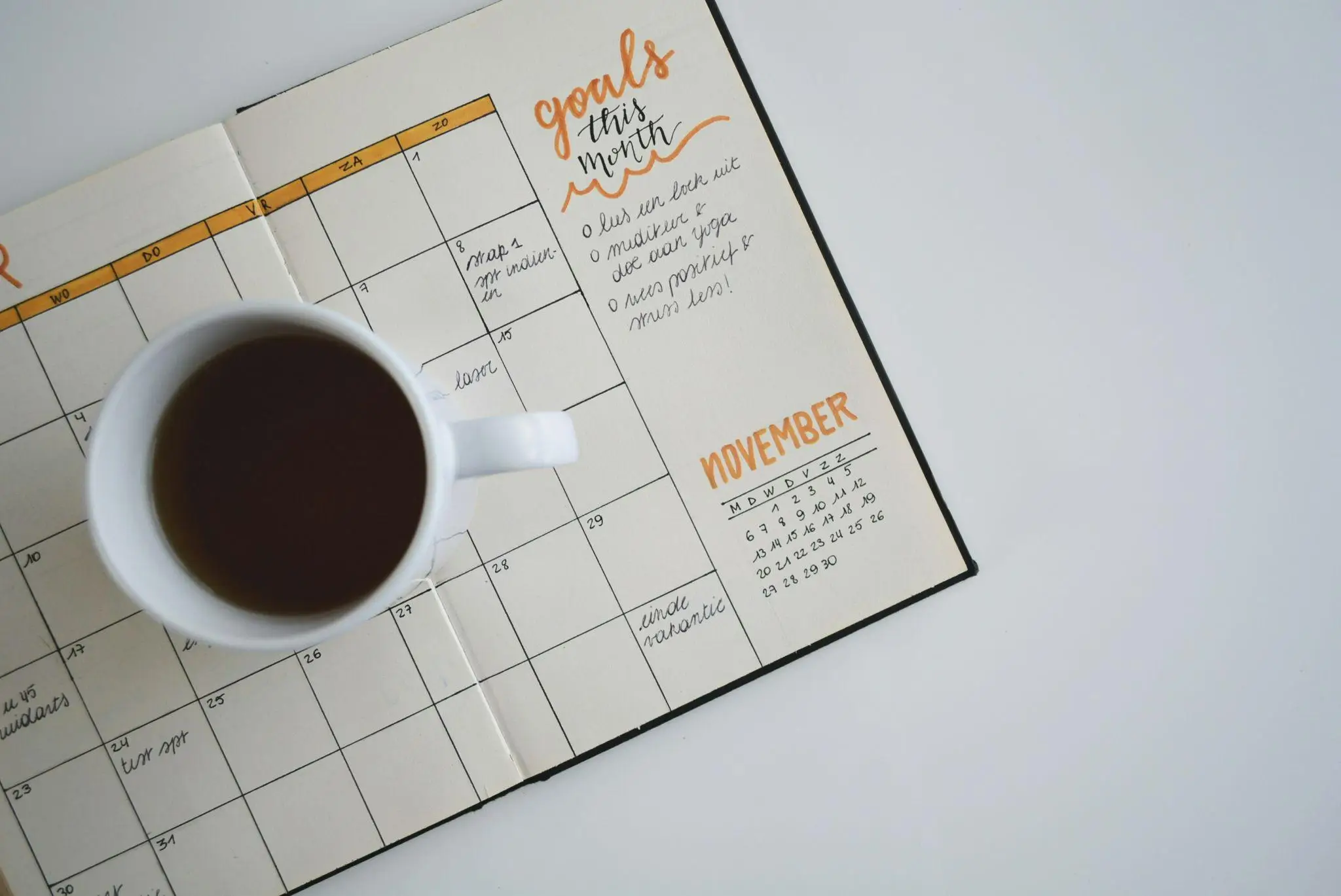 Open planner with handwritten notes and coffee cup on white table