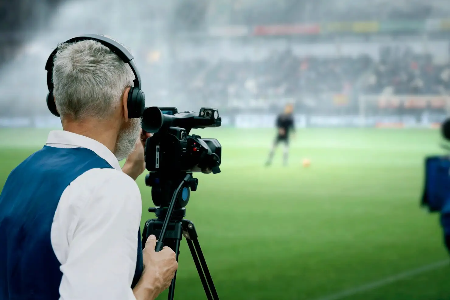 Cameraman with headphones filming soccer match on green field in stadium setting
