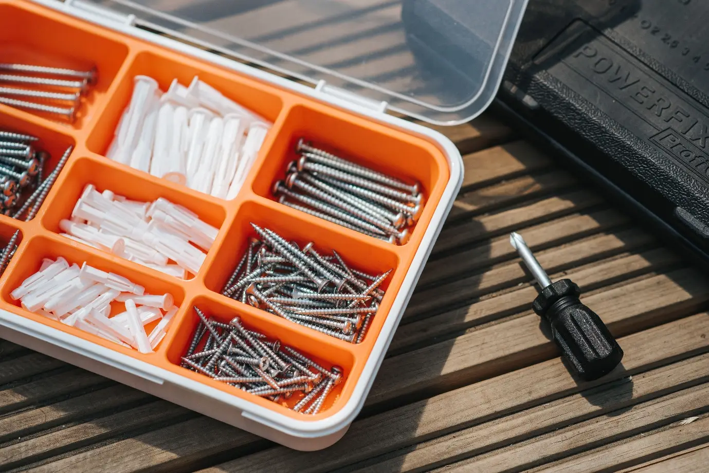 Plastic organizer box with screws and wall plugs on wooden surface in sunlight