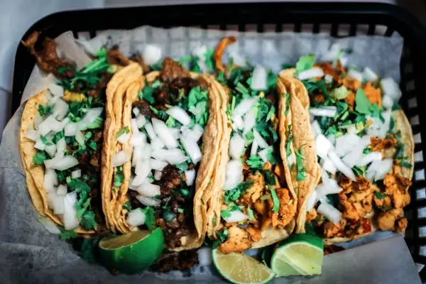 Four tacos with onions and cilantro in a basket with lime wedges