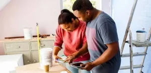 Couple examining paint samples on a table in a bright, partially renovated room